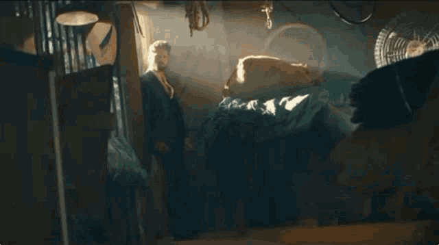 a man in a suit and tie is standing next to a bed in a dark room .