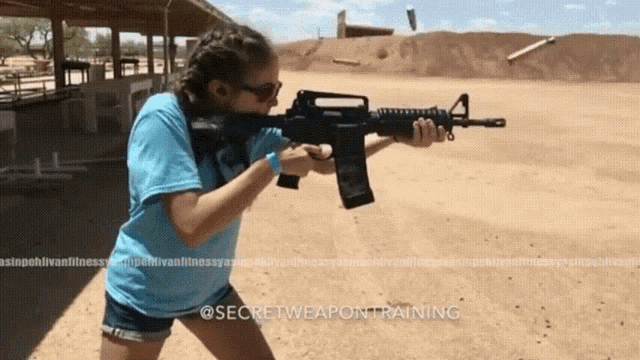 a woman in a blue shirt is holding an assault rifle at a shooting range sponsored by secretweapontraining