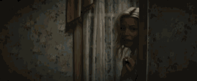 a woman looks out a window with a floral wallpaper