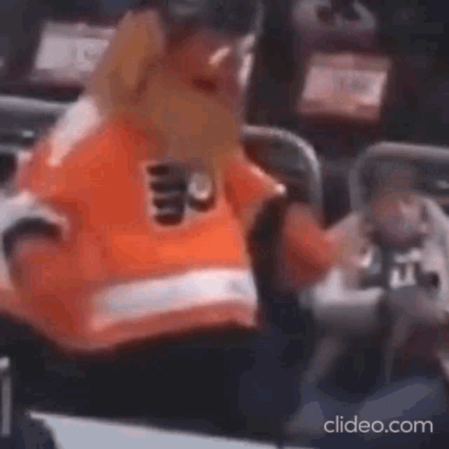 a man in an orange and white jersey is sitting in a chair .