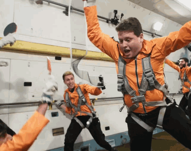 a man in an orange jacket is jumping in the air with his hands in the air