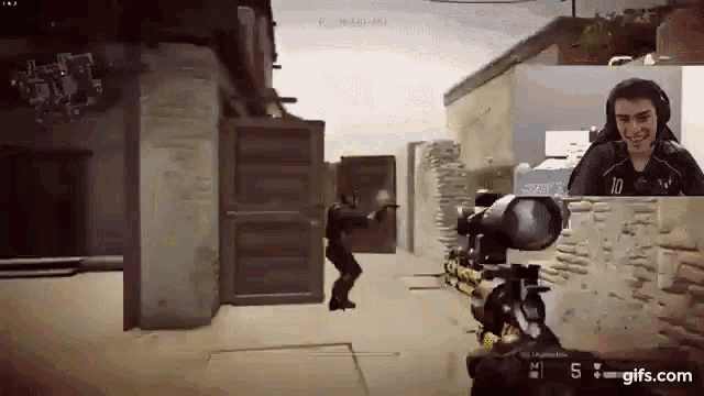 a man is playing a video game with a sniper rifle while another man looks on .