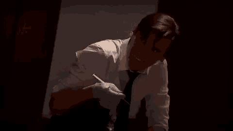a man in a white shirt and tie is holding a pair of gloves and a knife .