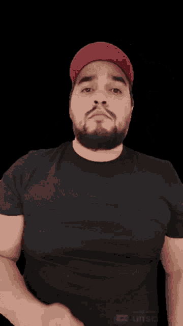 a man with a beard wearing a black shirt and a red hat giving a thumbs up