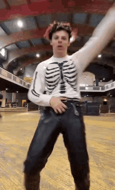 a man wearing a skeleton shirt and jeans is dancing on a roller rink .