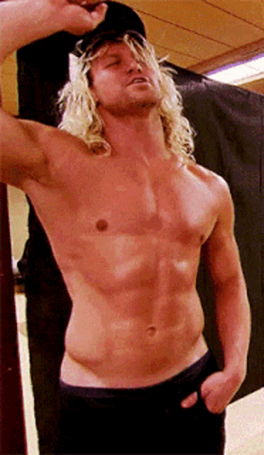 a shirtless man with long blonde hair is wearing a baseball cap