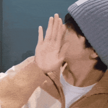 a man wearing a gray beanie covering his face with his hand