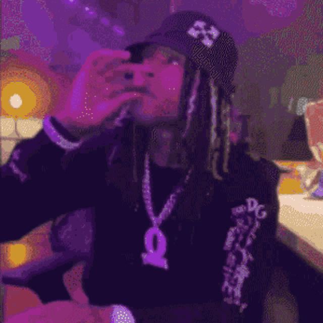 a man with dreadlocks wearing a hat and a necklace is drinking from a bottle .
