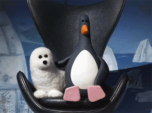 a stuffed seal and a stuffed penguin sit on a chair
