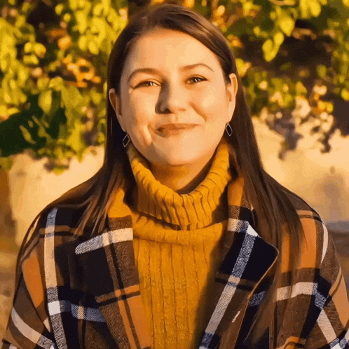 a woman wearing a plaid coat and a yellow sweater smiles