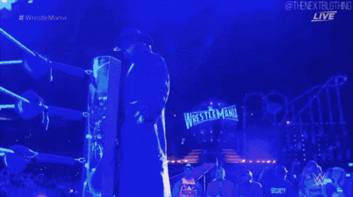 a wrestler is standing in front of a sign that says wrestlemania live