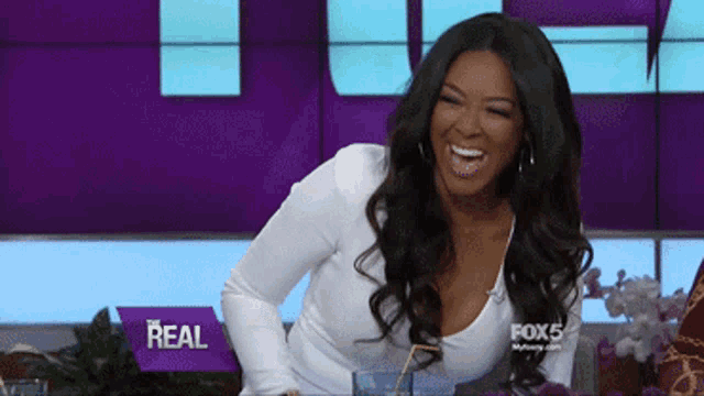 a woman laughs in front of a sign that says real