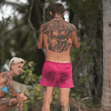 a man in pink shorts has a tattoo on his back of a skull