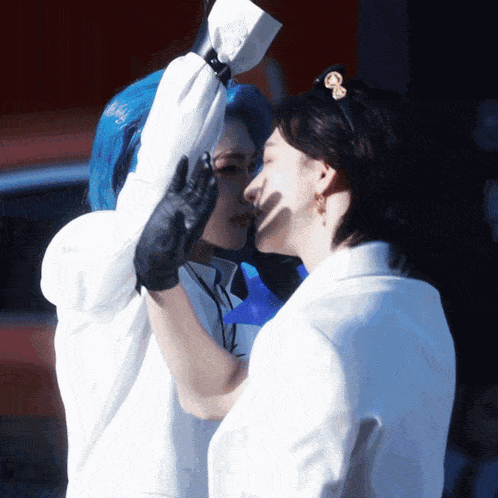 a woman with blue hair is kissing another woman in a white jacket