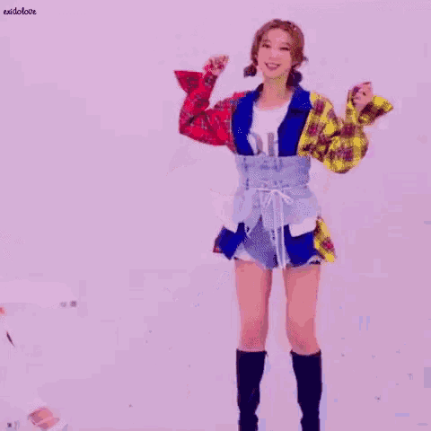 a woman in a plaid jacket and shorts is standing in front of a white wall with her arms outstretched .