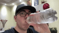 a man wearing glasses is drinking water from a plastic bottle .