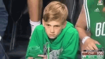 a young boy wearing a green hoodie is sitting in the stands watching a basketball game
