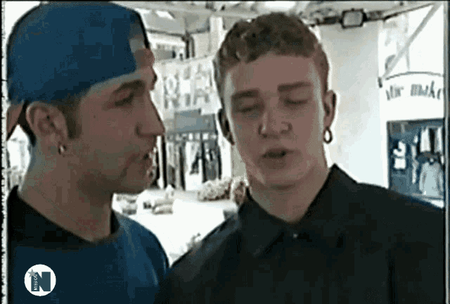 a man in a blue hat talks to another man in front of a sign that says mr. baker