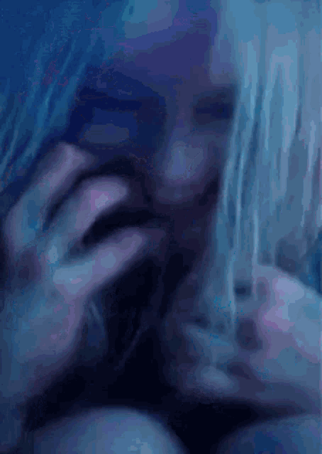 a close up of a woman 's face in a dark room with a blue and pink background .