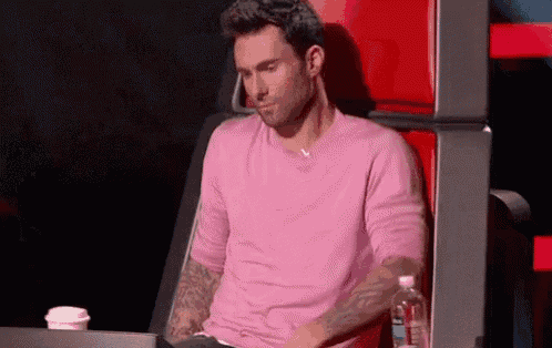 a man in a pink shirt is sitting in a chair with a bottle of water next to him .