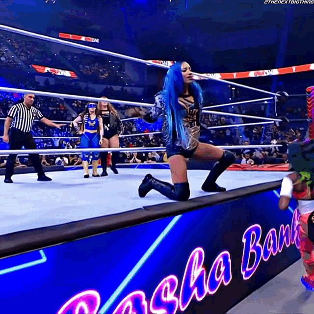 a woman with blue hair is kneeling on the edge of a wrestling ring in front of a sign that says sasha bank