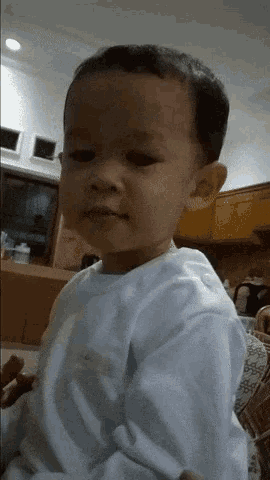 a little boy in a white shirt is looking at the camera with a serious look on his face
