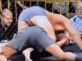 two men are wrestling in a boxing ring while a referee watches .