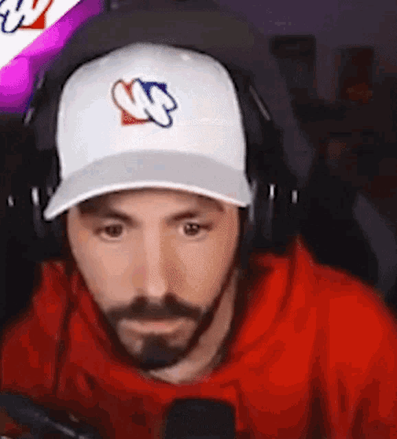 a man with a beard wearing a baseball cap and headphones is sitting in front of a microphone .