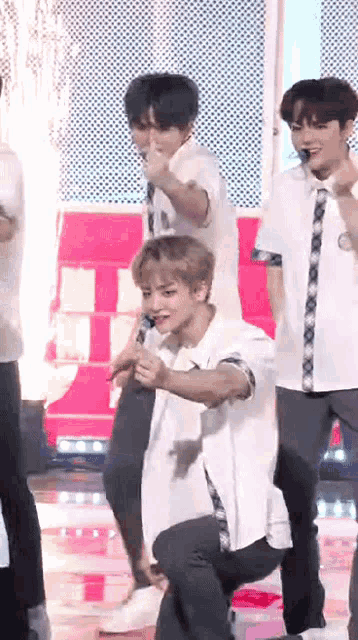 a group of young men are performing on a stage and one of them is kneeling down while holding a microphone .