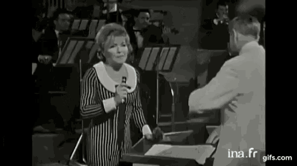 a woman singing into a microphone in front of an orchestra