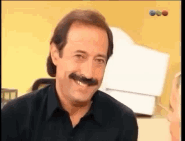 a man with a mustache and a black shirt smiles