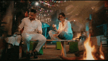 a man and a woman are sitting on a bench with a fire in the background .