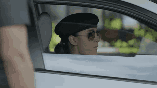 a woman in a beret and sunglasses is sitting in a car