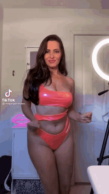 a woman in a pink bikini is standing in front of a mirror and a ring light .