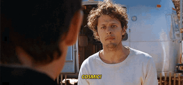 a man with curly hair is standing in front of an airstream and says cosmic