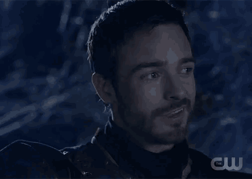 a man with a beard is smiling in the dark with a cw logo in the corner .