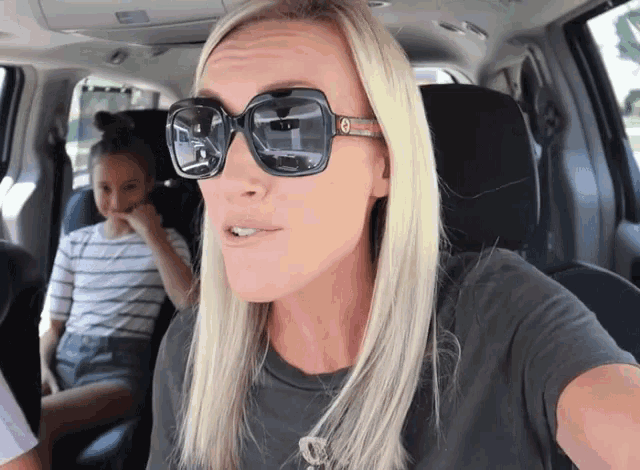 a woman wearing sunglasses is sitting in a car with a girl in the back seat