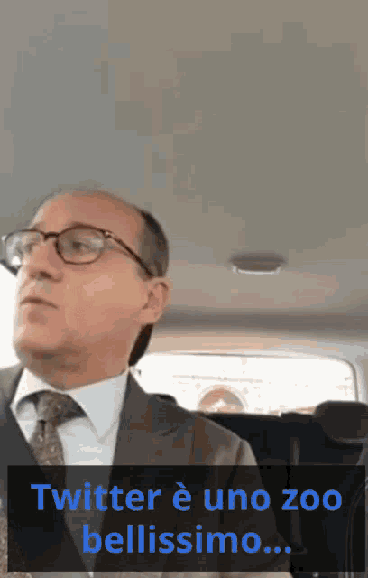 a man in a suit and tie is sitting in the back seat of a car with the words twitter è uno zoo bellissimo