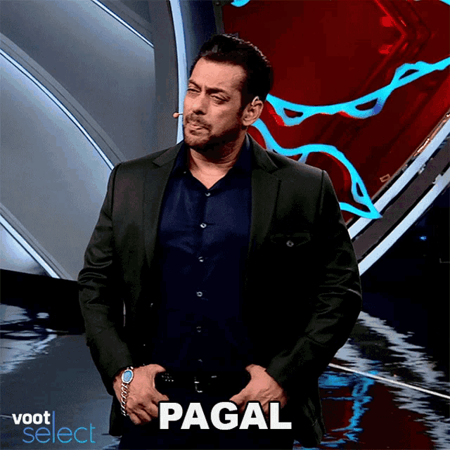 a man in a suit stands on a stage with his hands in his pockets and says " pagal " in front of him