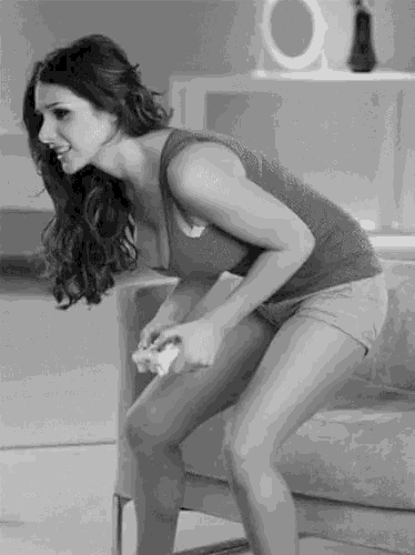 a woman in a tank top and shorts is squatting down while holding a remote control