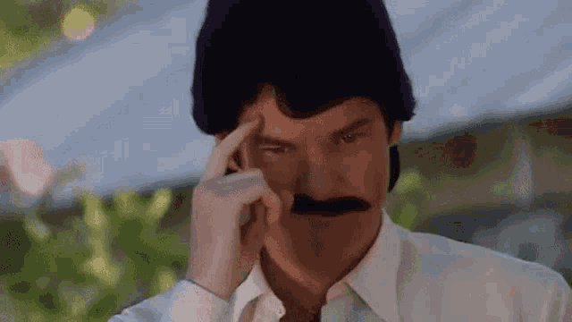 a man with a mustache is scratching his forehead .