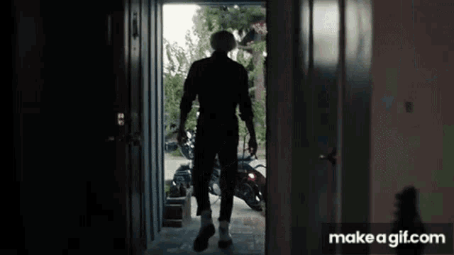 a man in a hat is walking out of a doorway with a motorcycle in the background .