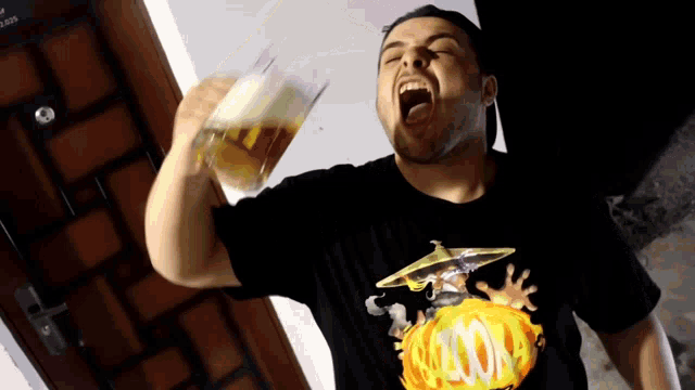 a man wearing a black shirt with a picture of a man with a hat and a fireball on it drinks from a glass
