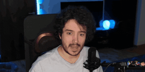 a man with a beard sits in front of a microphone and looks at the camera