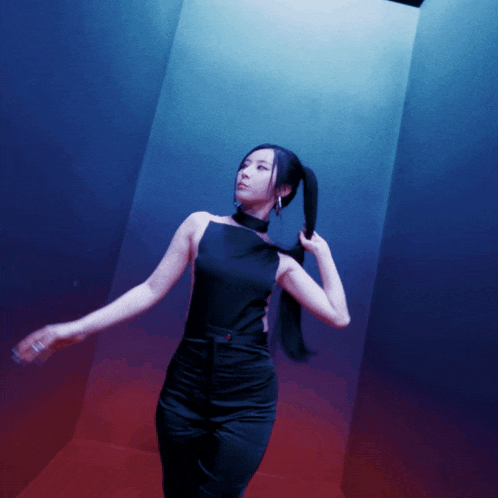 a woman in a black top and black pants stands in a dark room