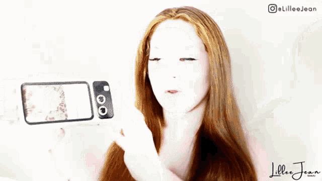 a woman with red hair is taking a selfie with her cell phone .