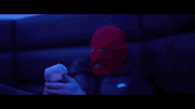 a man wearing a ski mask holds a stack of money