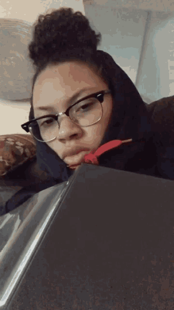a woman wearing glasses and a black hoodie is laying on a table