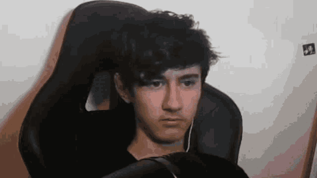 a young man is sitting in a gaming chair wearing headphones and looking at the camera .