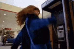 a woman in a blue jacket stands in front of a pay phone booth